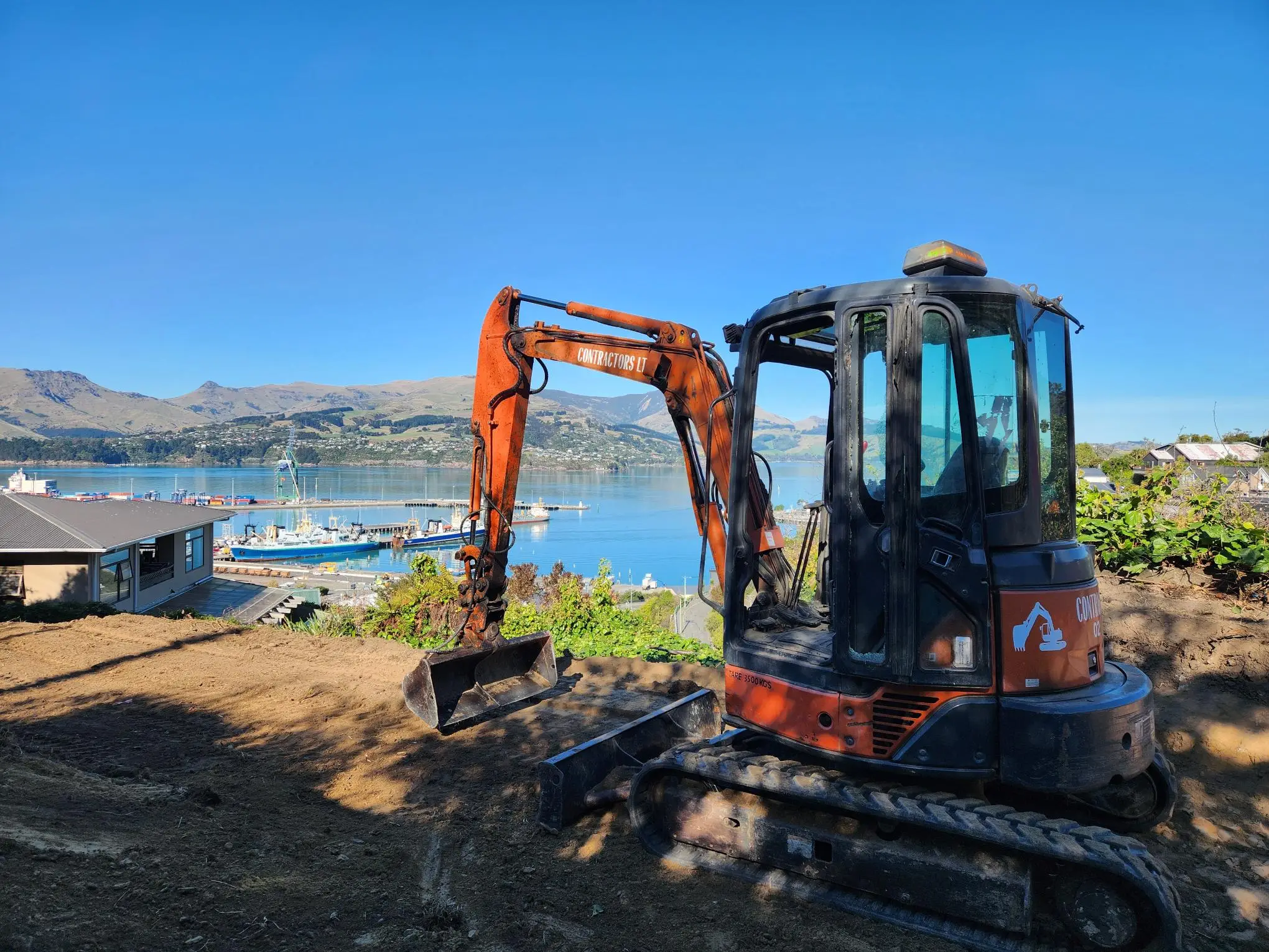 Digger on a hilltop site overlooking Lyttelton harbour and the Port Hills