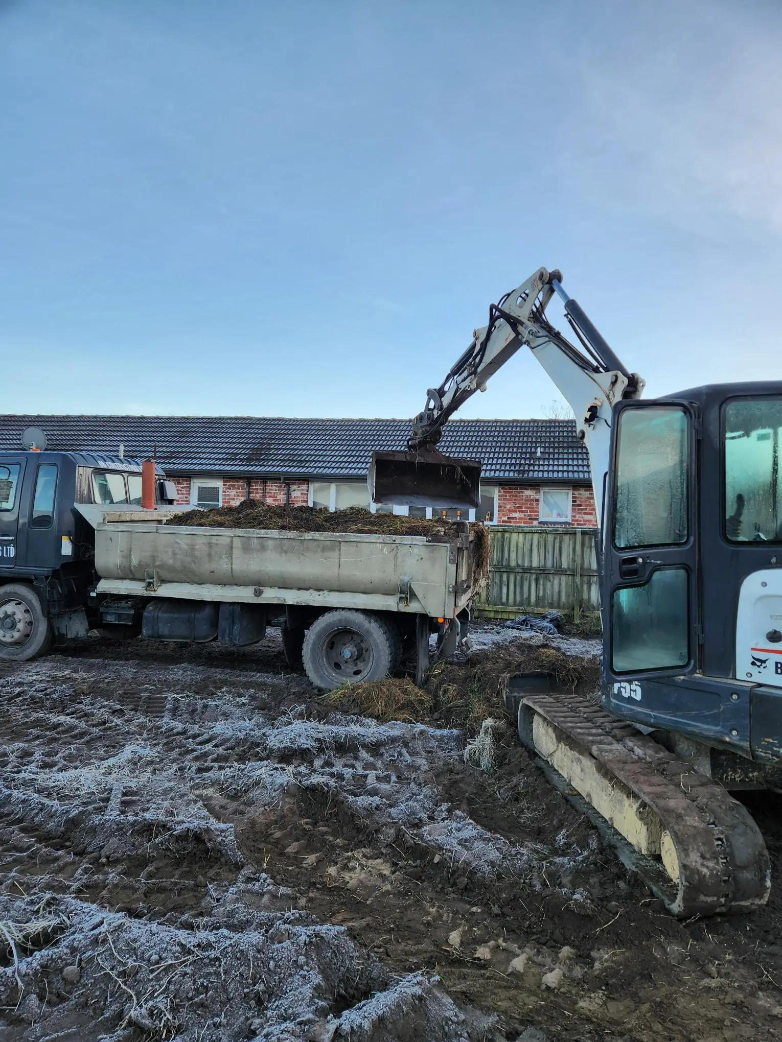 Digger loading a tipper truck with spoil at a residential site