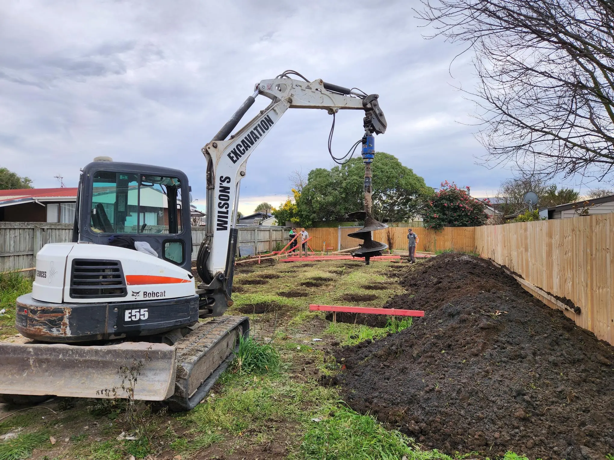 Bobcat mini digger with auger drilling post holes down a residential back garden