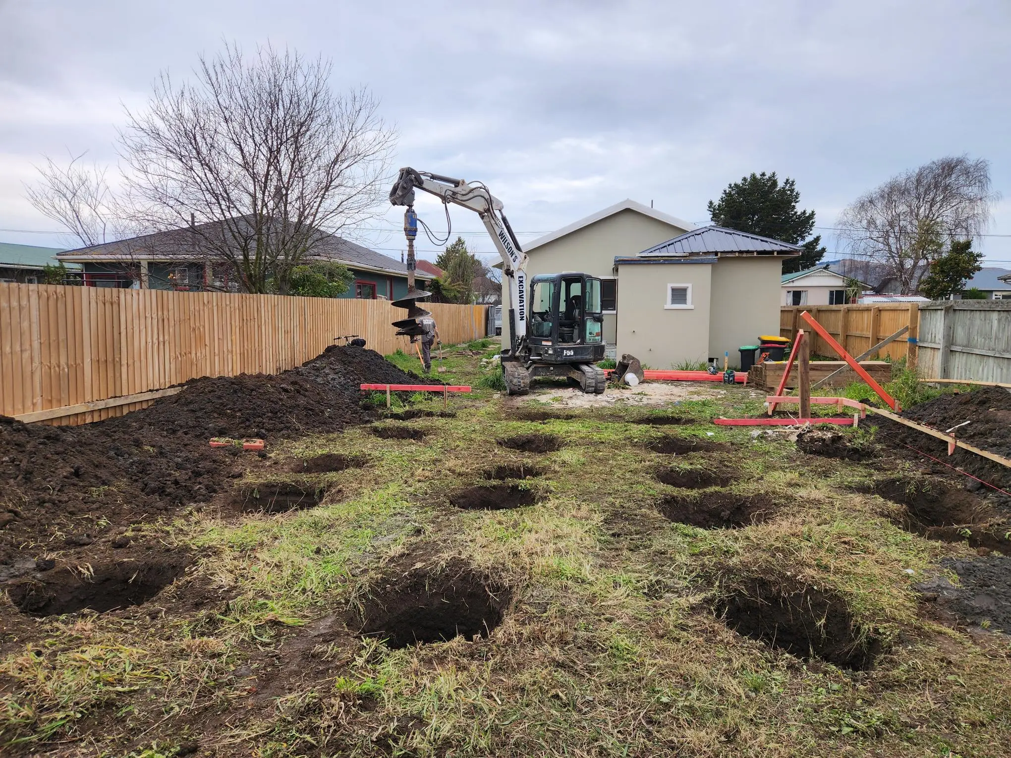 Bobcat mini digger with auger drilling post holes down a long residential back garden